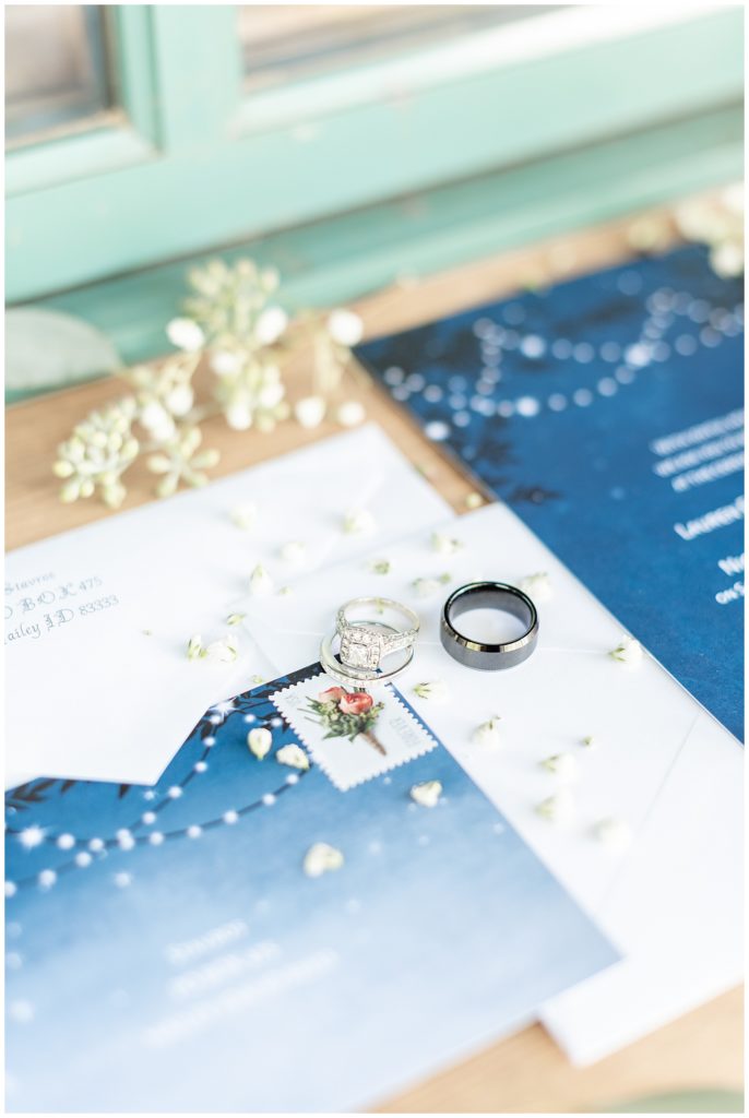 Sun Valley Wedding Photographer Denise and Bryan Photography, navy blue wedding invitations with floral stamps in window seal with rings. Wedding Flat lay with Invitation Suite
