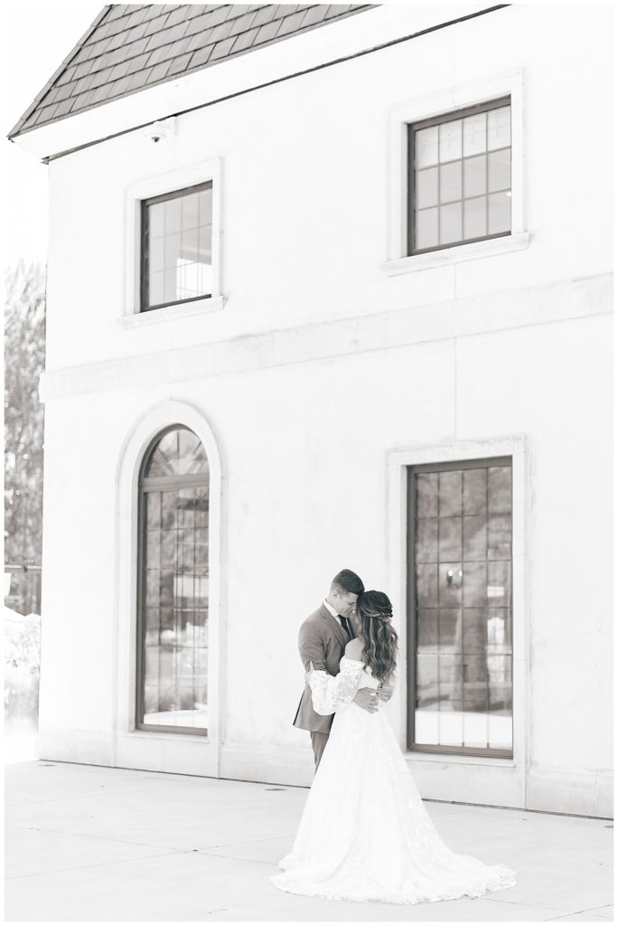Bride and groom posing next to a white stucco building at the Chateau Des Fleurs in Eagle, Idaho